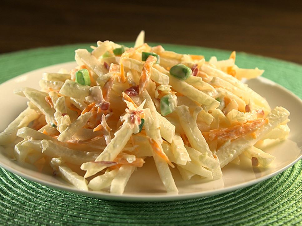 A white plate containing creamy jicama apple slaw sitting on a green placemat
